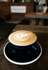 Cappuccino or latte with frothy foam, black coffee cup top on wooden coffee shop background