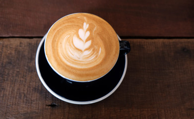 Cappuccino or latte with frothy foam, black coffee cup top on wooden coffee shop background