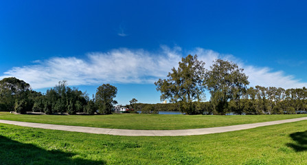 Beautiful panoramic view of a park with green grass, tall trees, walking trail and rainbow look-alike clouds, Reid Park, Parramatta Cycleway, Rydalmere, Sydney, New South Wales, Australia
