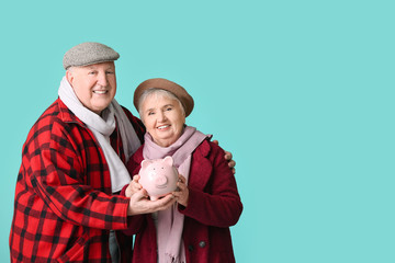 Happy senior couple with piggy bank on color background