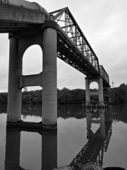 Beautiful black and white view of a river with reflections of a tall pedestrian and water pipe bridge, trees and sky on water, Parramatta river, Rydalmere, Sydney, New South Wales, Australia