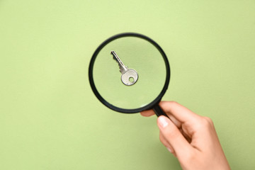 Female hand with magnifier and key on color background
