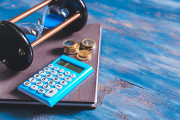 Hourglass with calculator and money on color wooden background