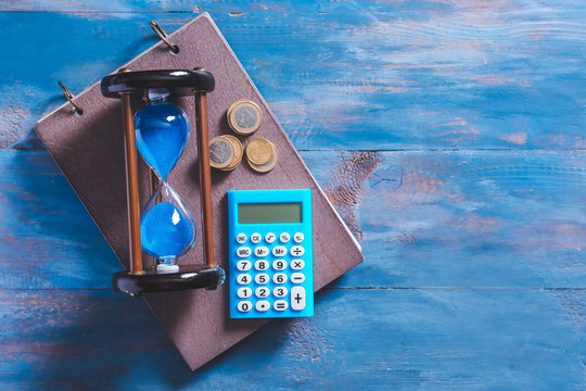 Hourglass with calculator and money on color wooden background
