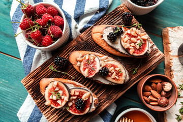 Obraz na płótnie Canvas Sandwiches with ricotta, fresh figs, berries, nuts and honey on rustic wooden board, blue background, top view