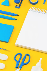 Assorted office and school white and blue stationery on bright yellow background. Organized...