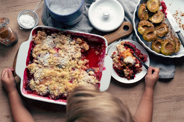 Little chef  tastes a homemade dessert with plum and fruit on wooden table.Delicious food made at home with healthy ingredient. Top view and close up. 