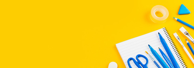 Assorted office and school white and blue stationery on bright yellow background. back to school or education and craft concept. Selective focus. Banner. Copy space