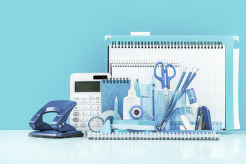 Grouped various office supplies and school white and blue stationery on desk. Blue background...