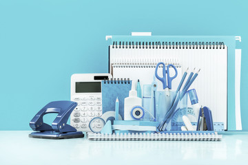Grouped various office supplies and school white and blue stationery on desk. Blue background monochrome. Poster for back to school or education and craft concept. Selective focus. Copy space