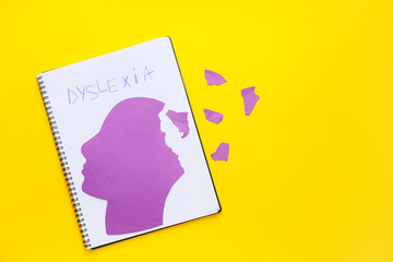 Notebook with word DYSLEXIA and paper human head on color background