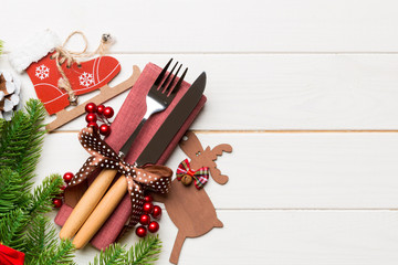 Fototapeta premium Top view of holiday objects on wooden background. Utensils tied up with ribbon on napkin. Christmas decorations and reindeer with copy space. New year dinner concept