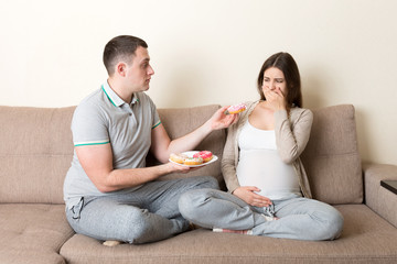Husband offers donuts to his pregnant wife but she refuses and makes stop gesture because she feels sick. Feeling bad during pregnancy concept