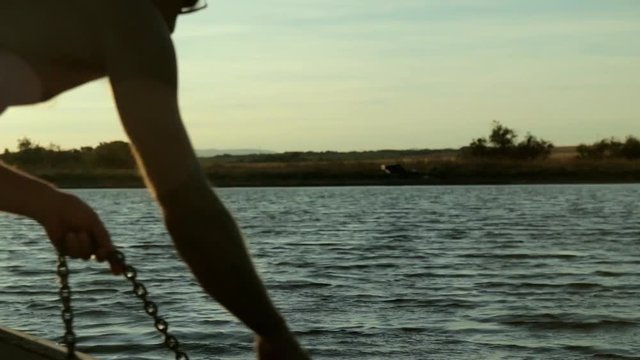 Un homme remonte une encre sur une barque au couch&eacute; du soleil.
