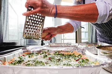 A woman makes spinach tomatoe quiche at home and grates parmesan cheese.