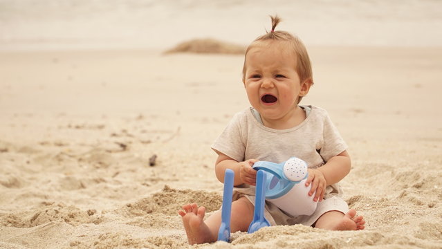 
Baby sitting on the sand cries. Bebé sentado en la arena quejándose