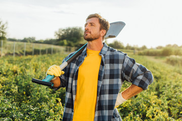 rancher in checkered shirt looking away while standing with hand on hip with shovel in field © LIGHTFIELD STUDIOS