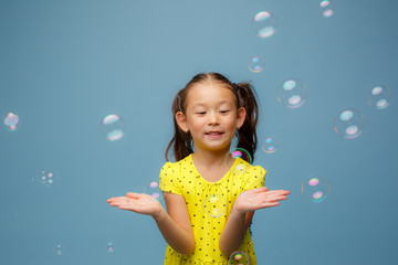 Asian girl playing with soap bubbles in the Studio on a blue background