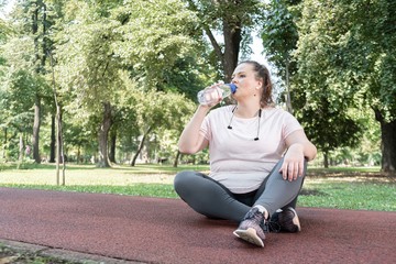 Plus size woman drinking water during outdoor workout