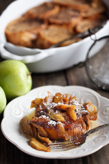 Serving of apple French toast casserole with maple syrup and powdered sugar. Selective focus with blurred background.