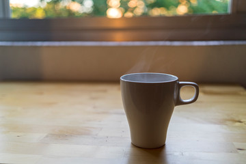 Taza de cafe saliendo humo frente a una ventana en una mesa d emadera