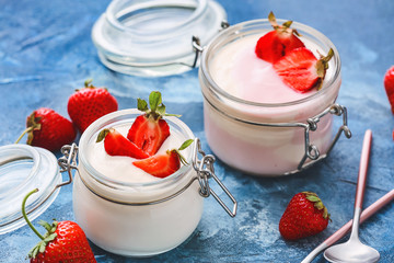 Jars of strawberry yogurt on color background