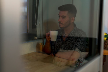 Joven con taza de cafe trabajando en el ordenador junto a la ventana