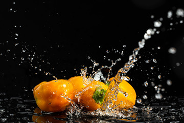 Naklejka na ściany i meble Sweet peppers on a black background with drops and splashes of water
