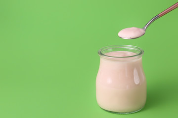 Jar of strawberry yogurt on color background