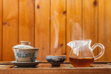 Dishes for traditional chinese tea ceremony with splashing hot water and a cloud of steam on a wooden background