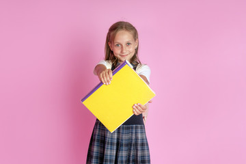 Fototapeta na wymiar A charming girl with blond hair in a school uniform with a book in her hands on a pink background. Studio photo. Back to school