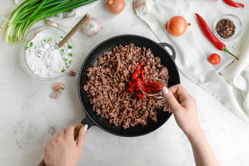 Woman preparing tasty beef casserole on light background, top view