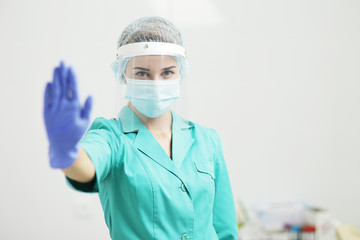 Fototapeta na wymiar A Female doctor or nurse in uniform, medical mask, protective shield, and gloves shows stop gesture with hand. Coronavirus Covid-19. Girl, woman.
