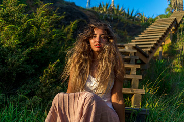 Chica joven posando en unas escaleras de madera al tardecer en la playa