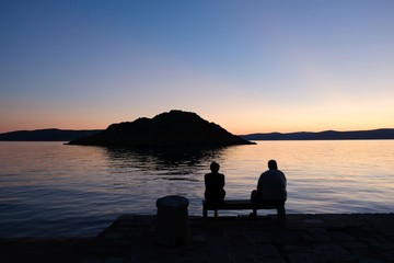 Obraz premium Black silhouettes of people against the background with sunset by the sea. There is island on horizon.