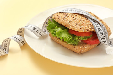 Plate with sandwich and measuring tape on color background. Concept of anorexia