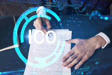 Businessman in suit signs white papper. Double exposure with ICO icon hologram. Man signing contract agreement. Blockchain market analysis and investment concept.