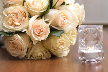 A bouquet of white roses and a crystal box with wedding rings on a wooden table