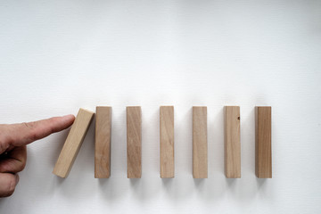 A finger pushes wooden dominoes on a white isolate, place for a photo