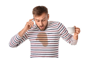 Naklejka premium Stressed young man with coffee stains on his t-shirt talking by mobile phone on white background