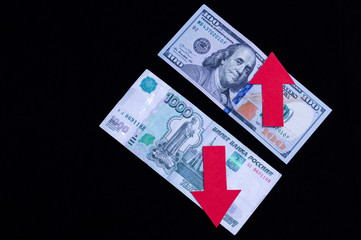one hundred dollar bill on a black background with a red up arrow and a thousand russian rubles with a red down arrow on a black background.Concept of crisis, falling economies of developing countries