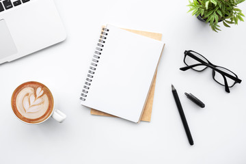 Blank notebook with pen are on top of white office desk table with laptop computer, cup of latte...