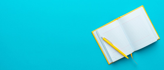 Top view photo of opened notebook and yellow pen over it on turquoise blue background with copy space. Minimalist flat lay image of blank diary and ball-point pen