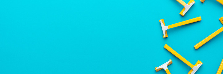 Many disposable unisex razors on the turquoise blue background. Top view of yellow plastic razors with copy space