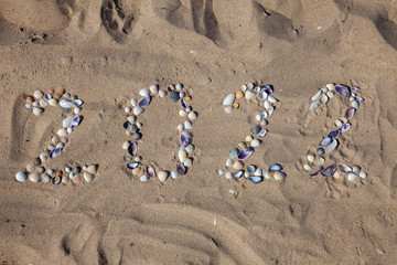 Fototapeta na wymiar The numbers 2022 are written and lined with seashells in the sand. New year on the beach. Sea coast. Place for your text. Summer in winter. Natural background.