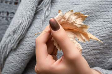 Female hand with brown nail design. Brown nail polish manicured hand. Woman hand hold yellow autumn leaf.