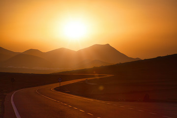 Fototapeta premium Auf der Kanarischen Insel Lanzarote führt diese Straße dem Sonnenuntergang entgegen zu den Vulkanen
