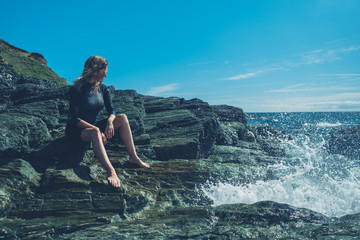 Young woman sitting on rocks by sea with waves crashing in