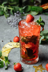Strawberry Mojito. Cold summer mojito cocktail with strawberries, mint, lemon and ice in a glass on a table. on a dark background