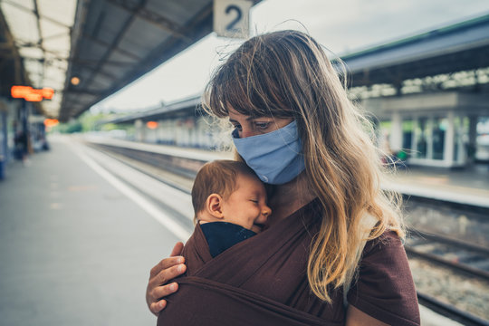 Young mother with baby in sling wearing face mask at train station